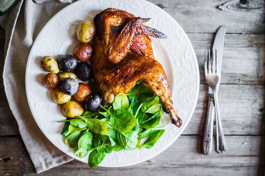 Half a grilled chicken with roast potatoes and spinach (seen from above)