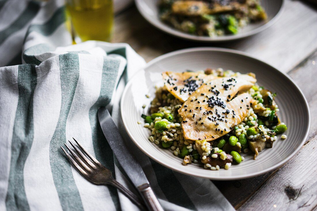 Grilled fish fillet with mushroom risotto and edamame beans on a rustic surface