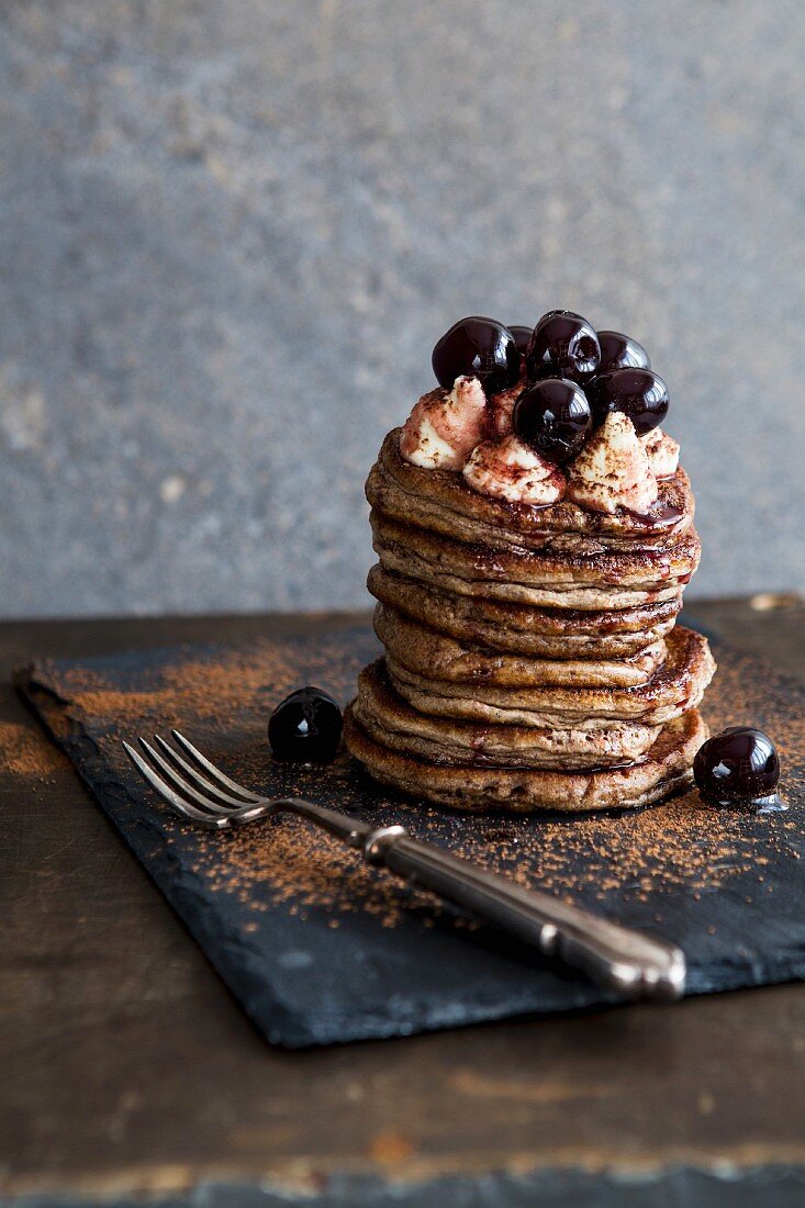 A stack of pancakes with cherries and cream