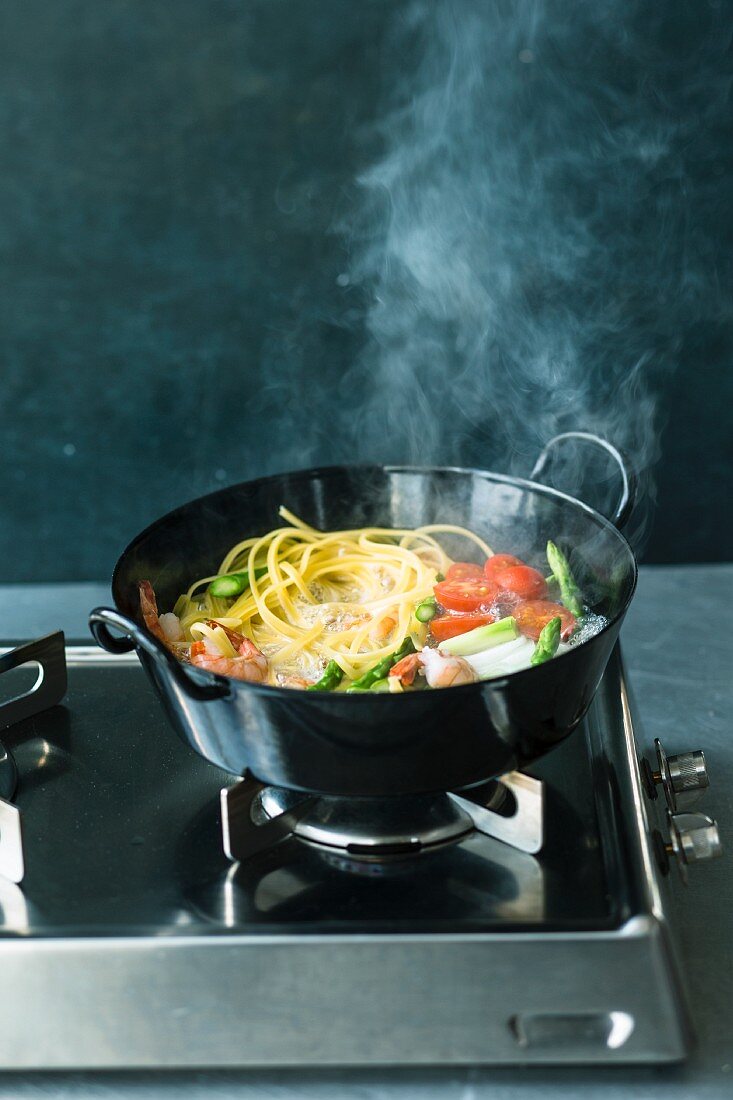 Linguine mit Tomaten und Garnelen im dampfenden Kochtopf