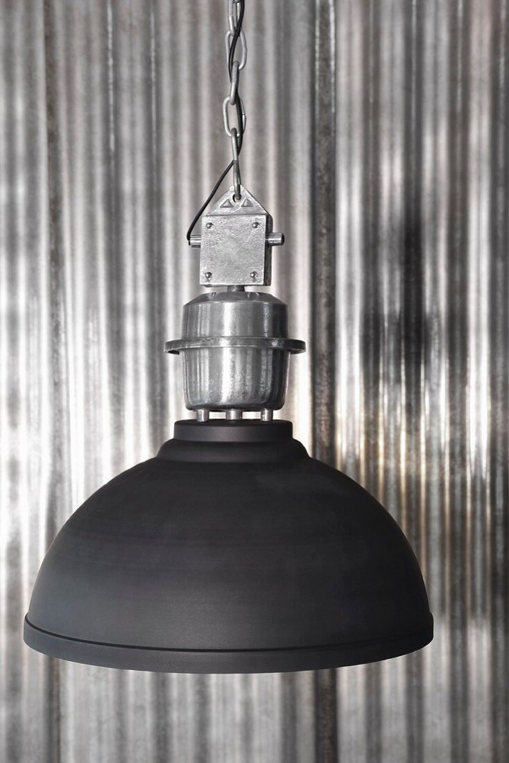 Black industrial-style lampshade against shiny corrugated metal wall