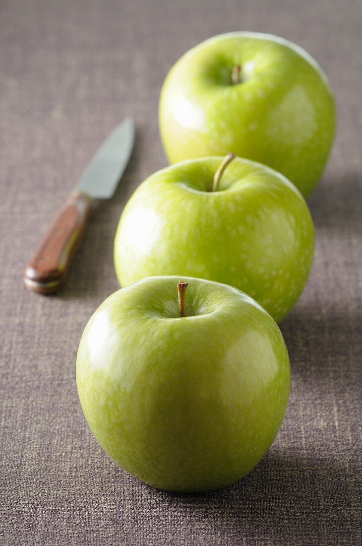 Drei grüne Äpfel auf grauem Tischtuch