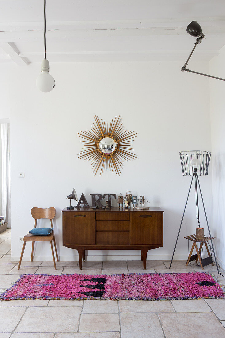 Retro Sideboard aus Edelholz, darüber Wandspiegel in Strahlenform und verschiedene Lichtquellen an Wand und Decke