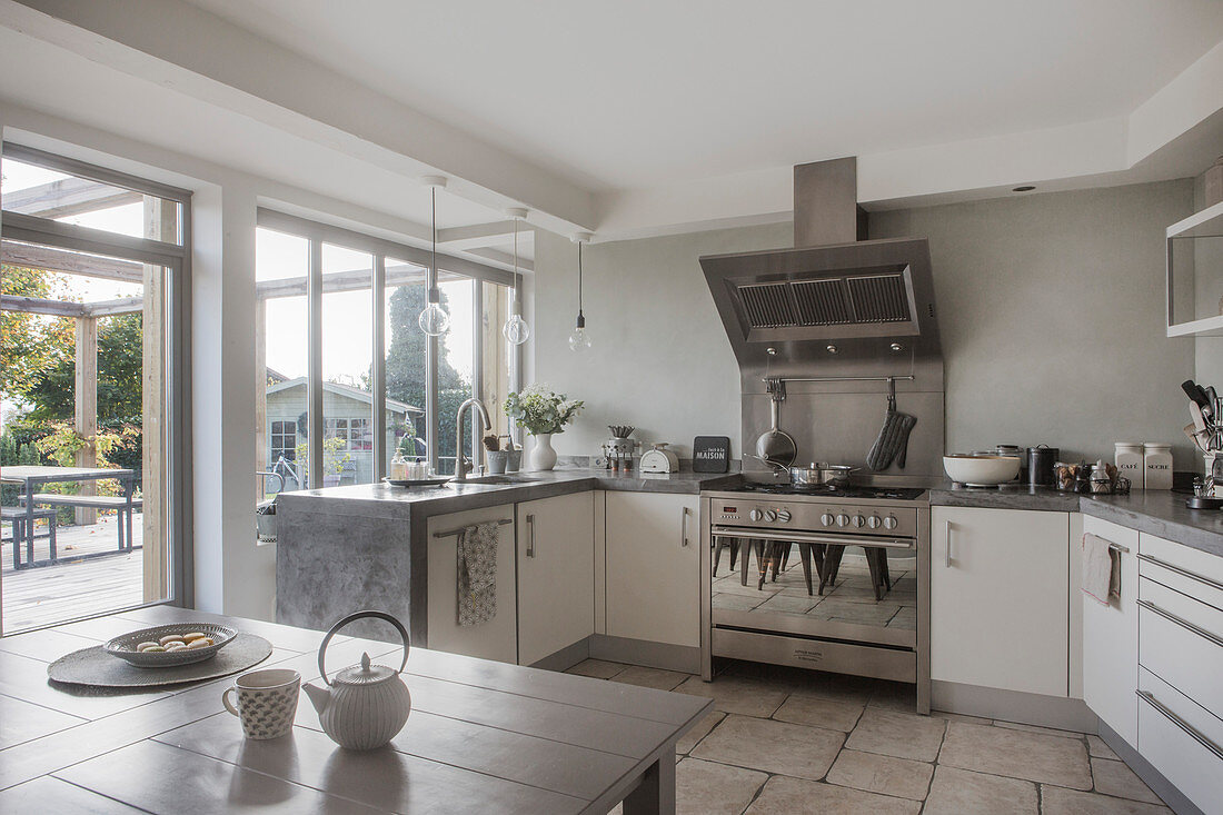 White, U-shaped kitchen counter with concrete worksurface and view of terrace