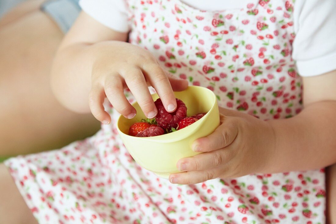 Kinderhand greift in Schale mit frischen Beeren