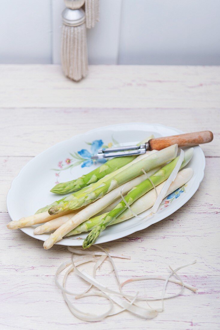 Green and white asparagus with a peeler and peelings on a porcelain plate