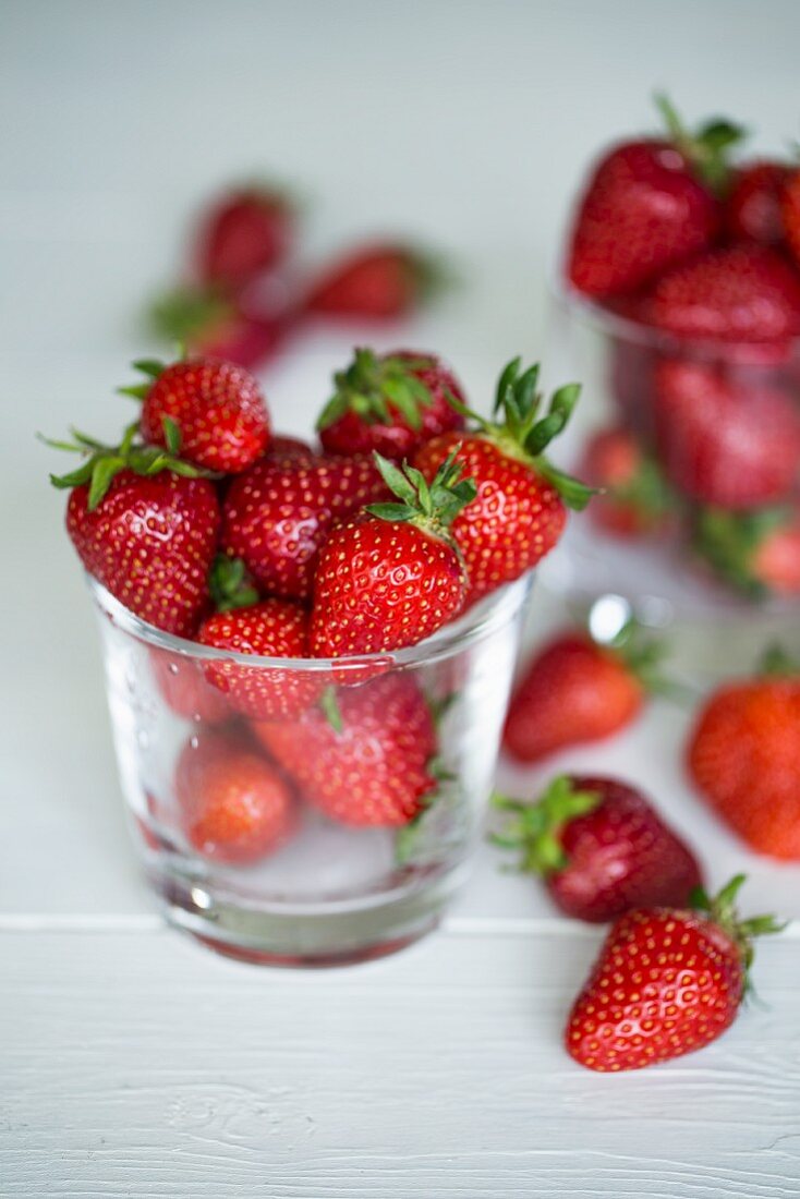Freshly washed strawberries in a glass on a white wooden surface