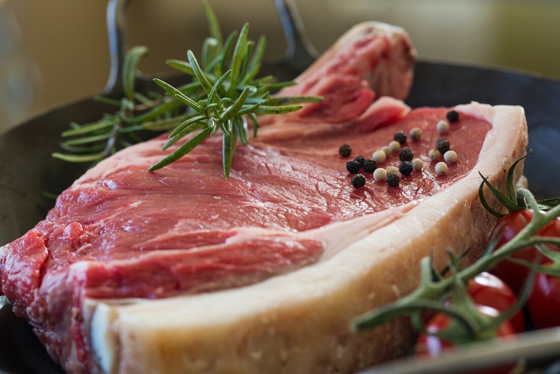 Cote de boeuf in a cast iron pan with tomatoes, rosemary and peppercorns