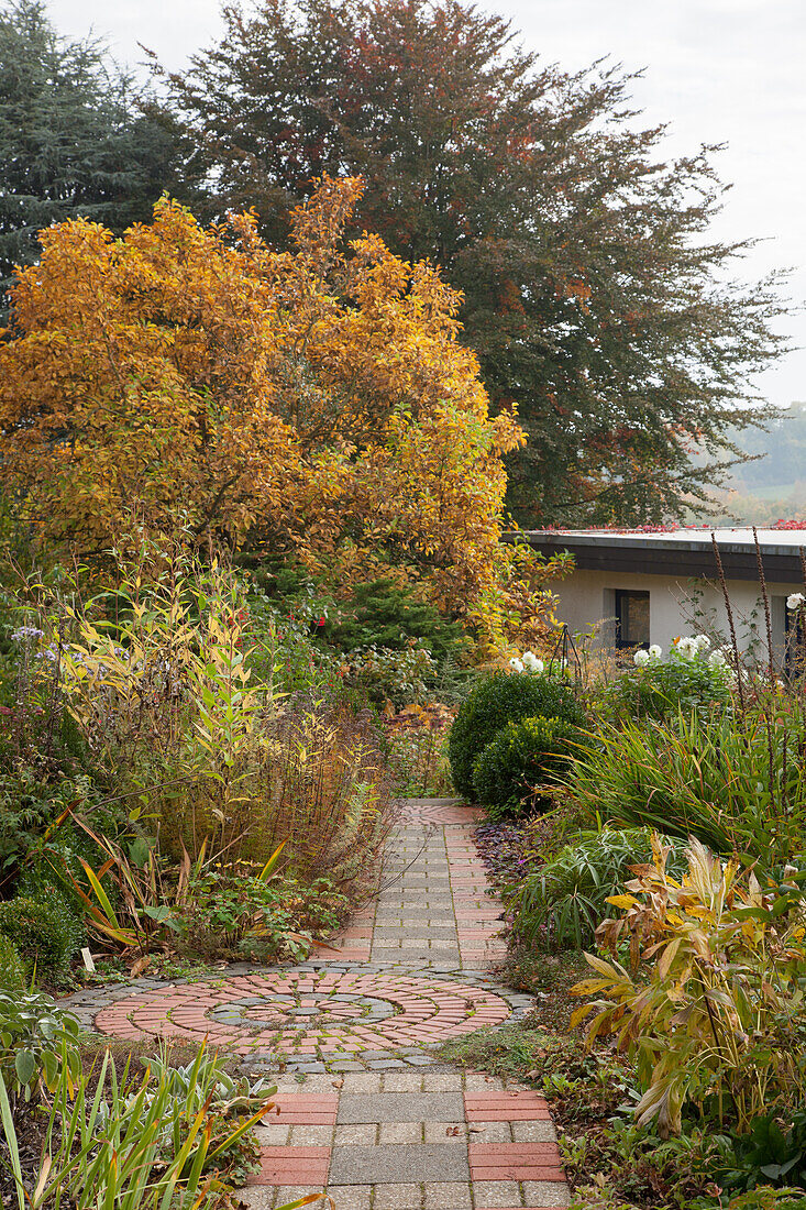 Pflastersteinweg durch einen herbstlichen Staudengarten