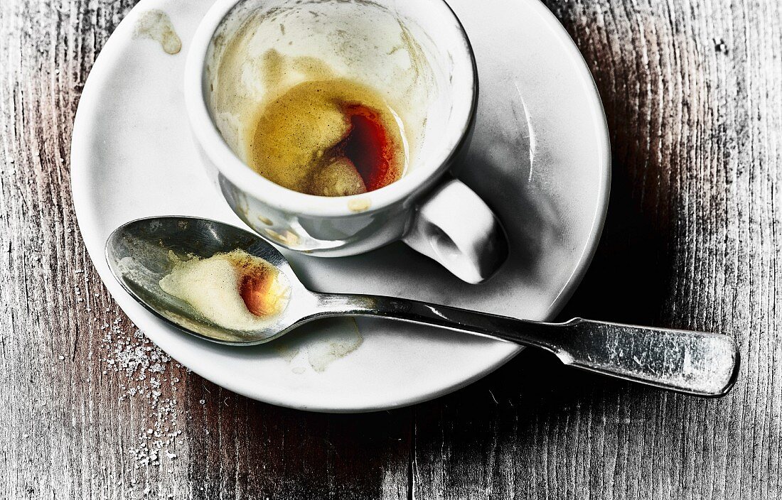 The remains of coffee in an espresso cup and on a spoon on a saucer