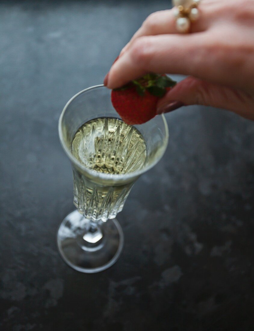 Frauenhand legt Erdbeere in ein Glas Prosecco