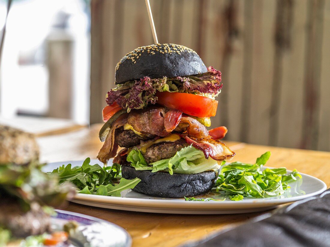 A black bread double burger with bacon, lettuce and cheese on a wooden skewer