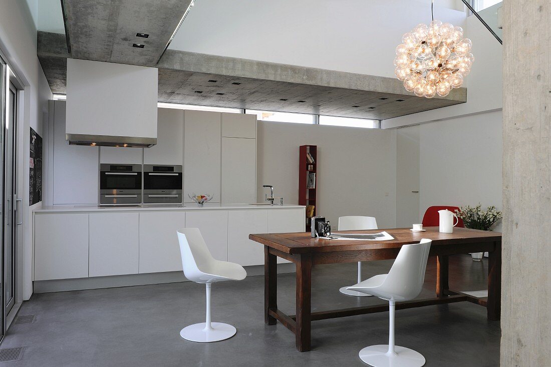 White shell chairs around rustic wooden table in open-plan kitchen with concrete ceiling