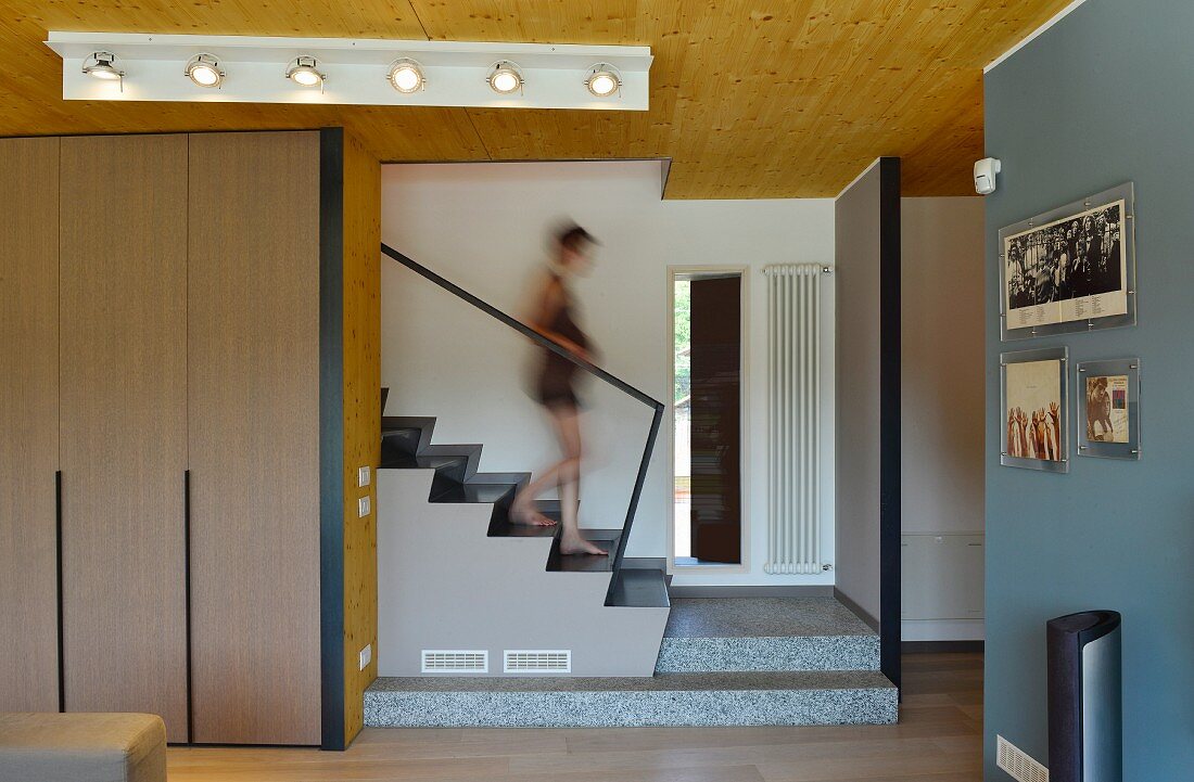 Woman walking down staircase into living area with fitted cupboards and open doorway