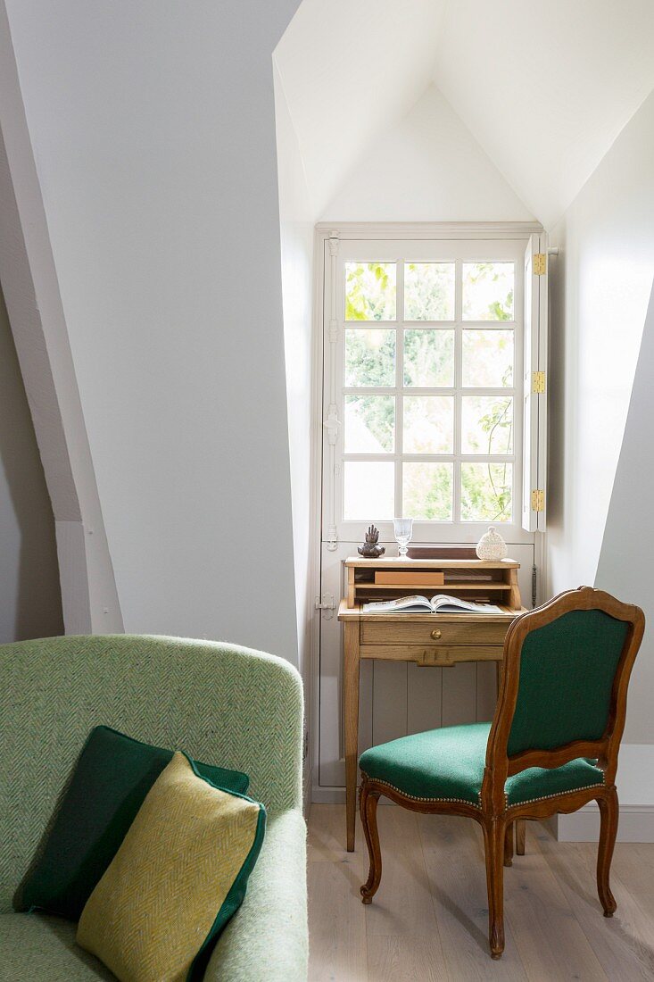 Writing desk and antique upholstered chair in niche below lattice dormer window