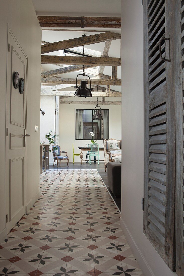 Ornamental floor tiles in hallway and view into open-plan interior with rustic half-timber beams