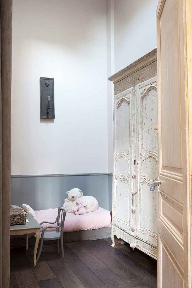 View through open door of child's chair, table, bed and wardrobe in child's bedroom