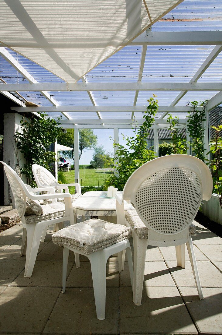 White plastic chairs and stools with seat cushions below awning in conservatory