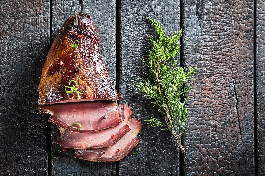 Smoked ham with a sprig of juniper on a scorched tabletop