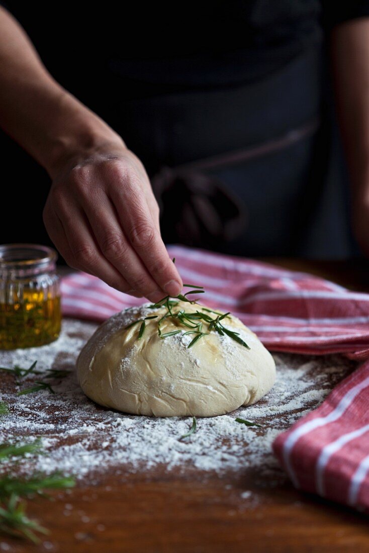 Bread dough being sprinkled with rosemary