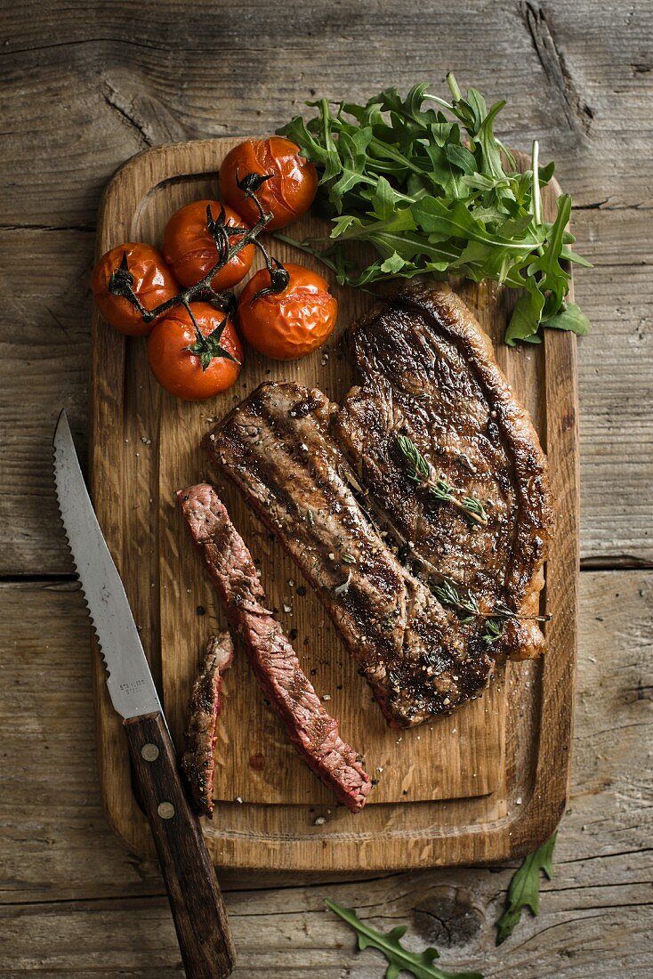 Grilled beef steak with tomatoes and rocket on a chopping board