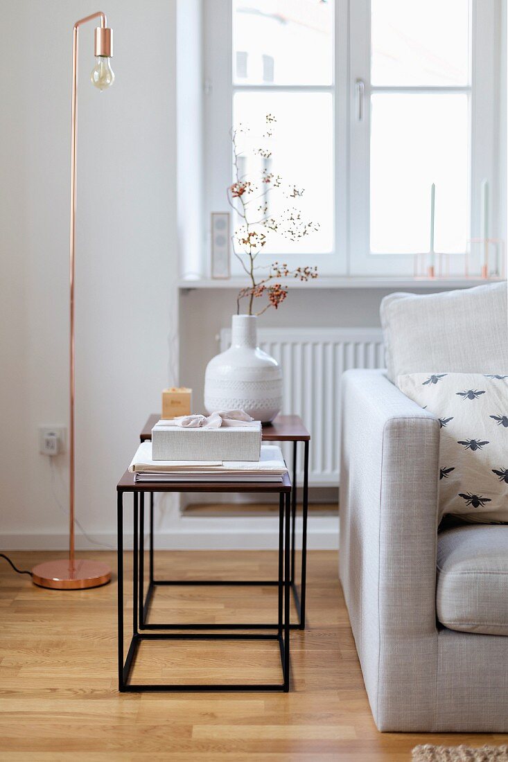 Delicate side tables and copper lamp next to sofa