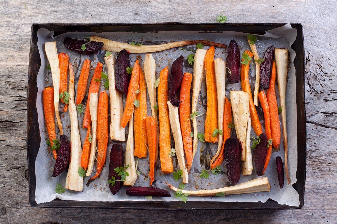 Roasted root vegetables and beetroot on a baking tray (seen from above)