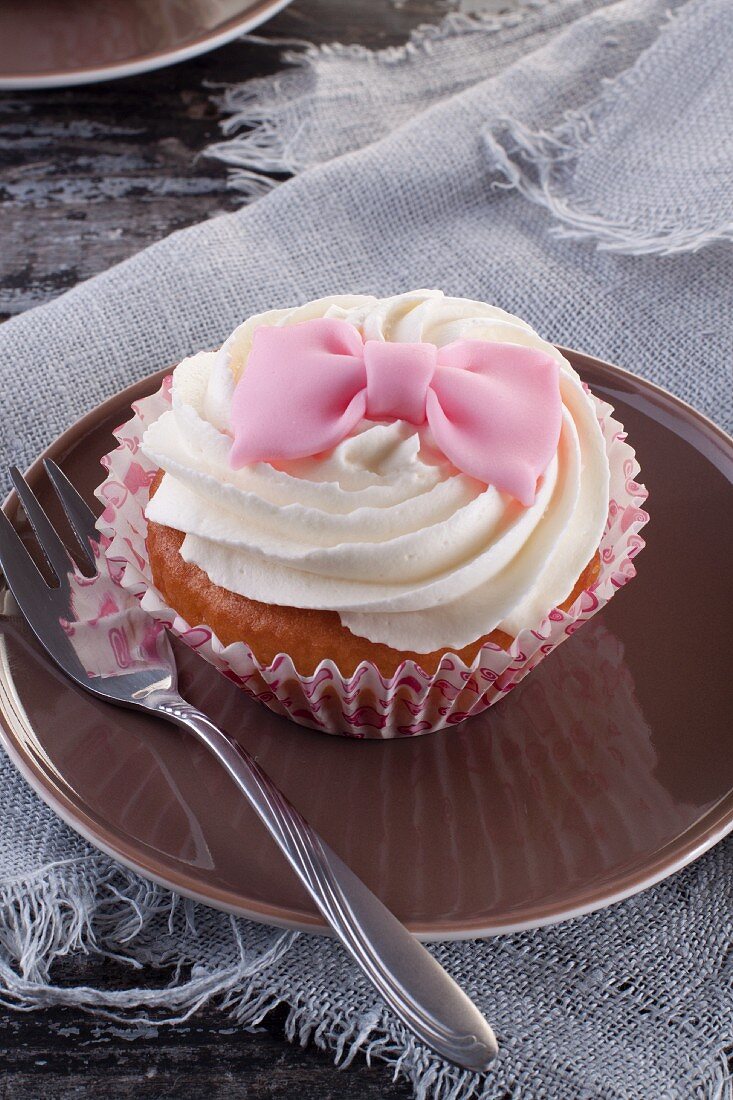 A cupcake decorated with a pink fondant bow