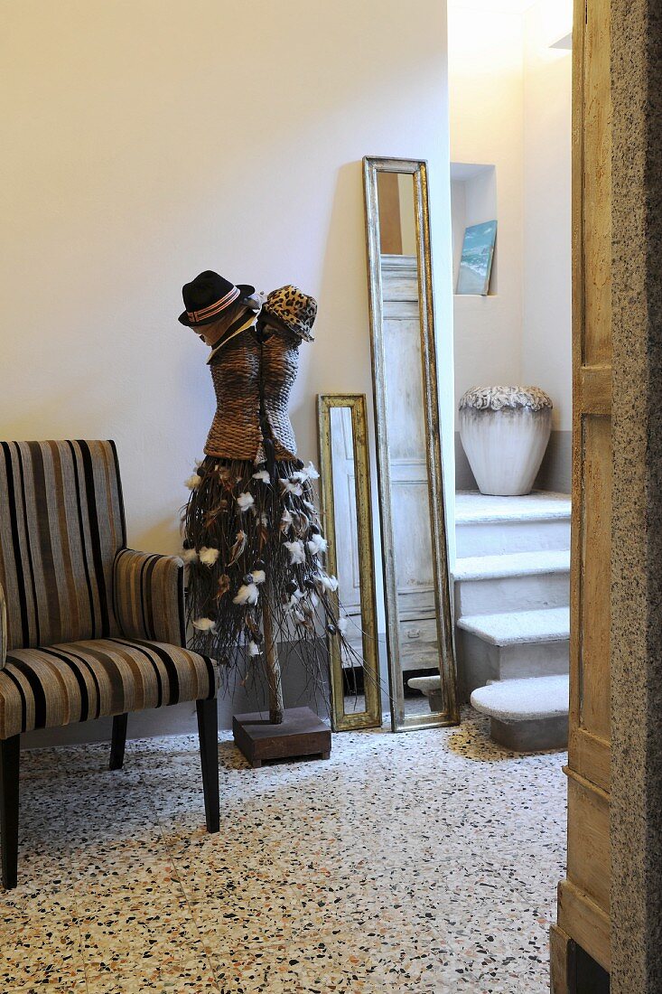 Sculpture with hats next to striped armchair on terrazzo floor tiles and foot of staircase