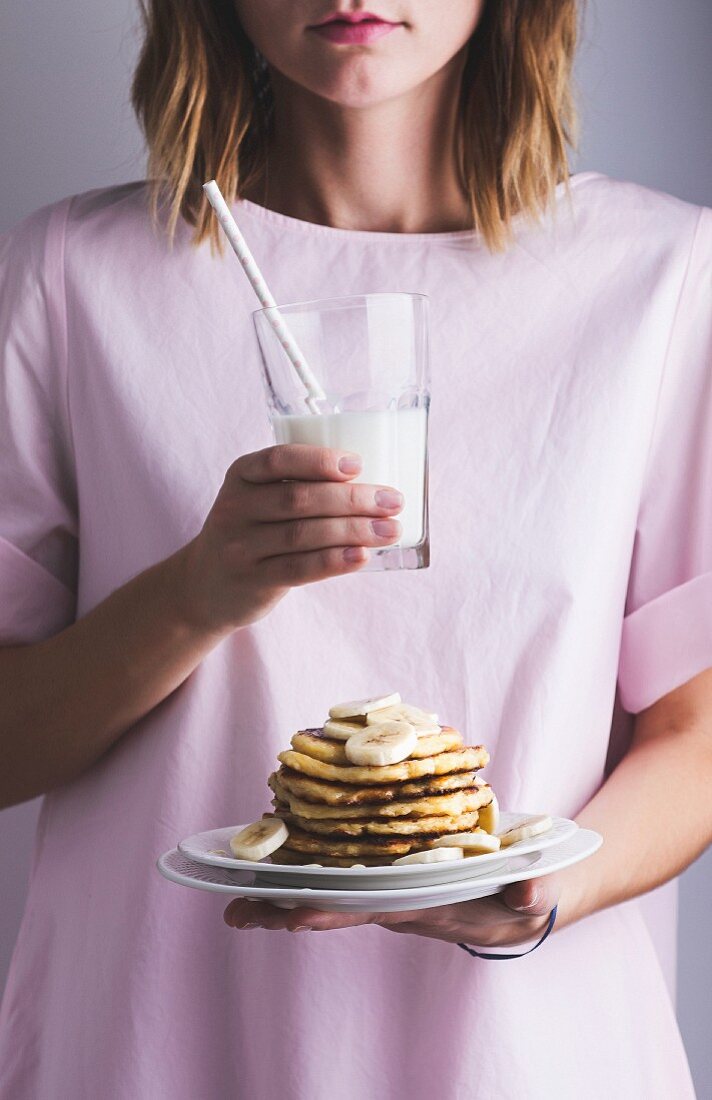 Mädchen hält Teller mit Pancakes und Bananen sowie ein Glas Milch