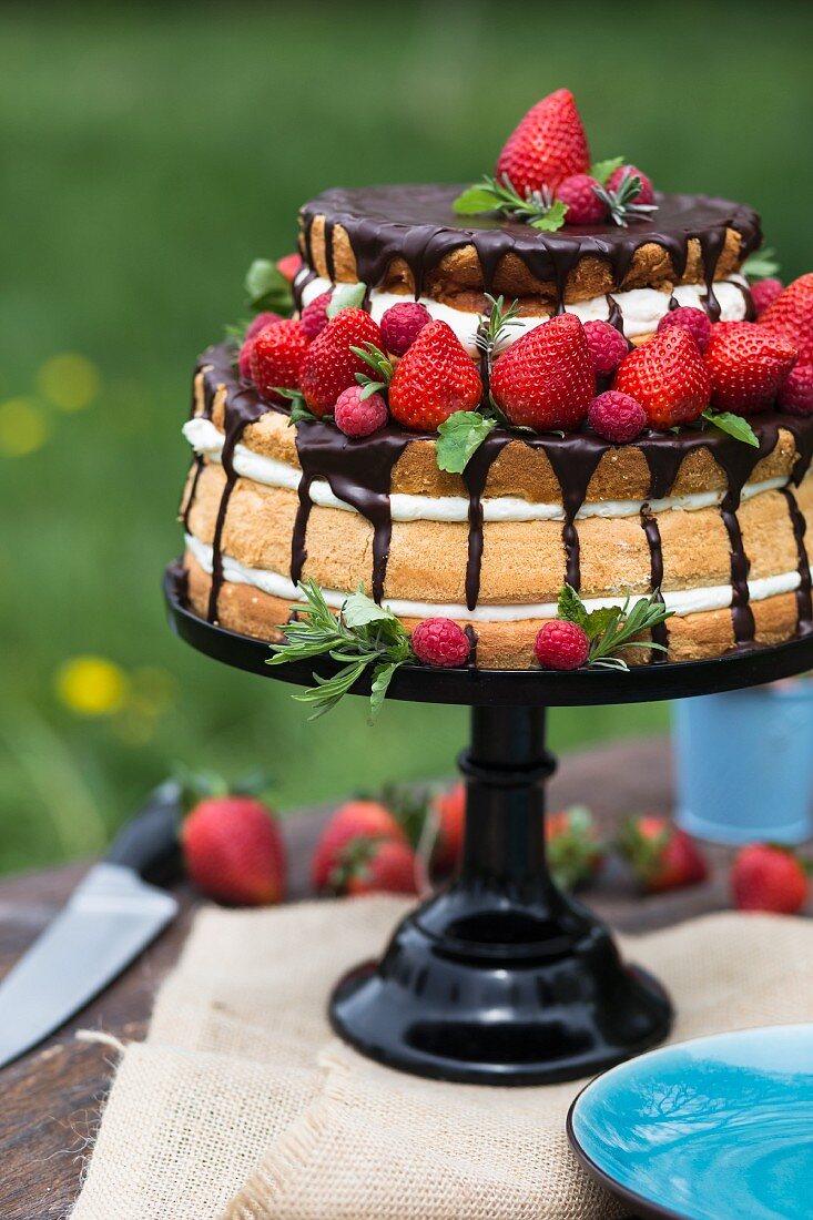 A naked cake with strawberries, cream and chocolate glaze