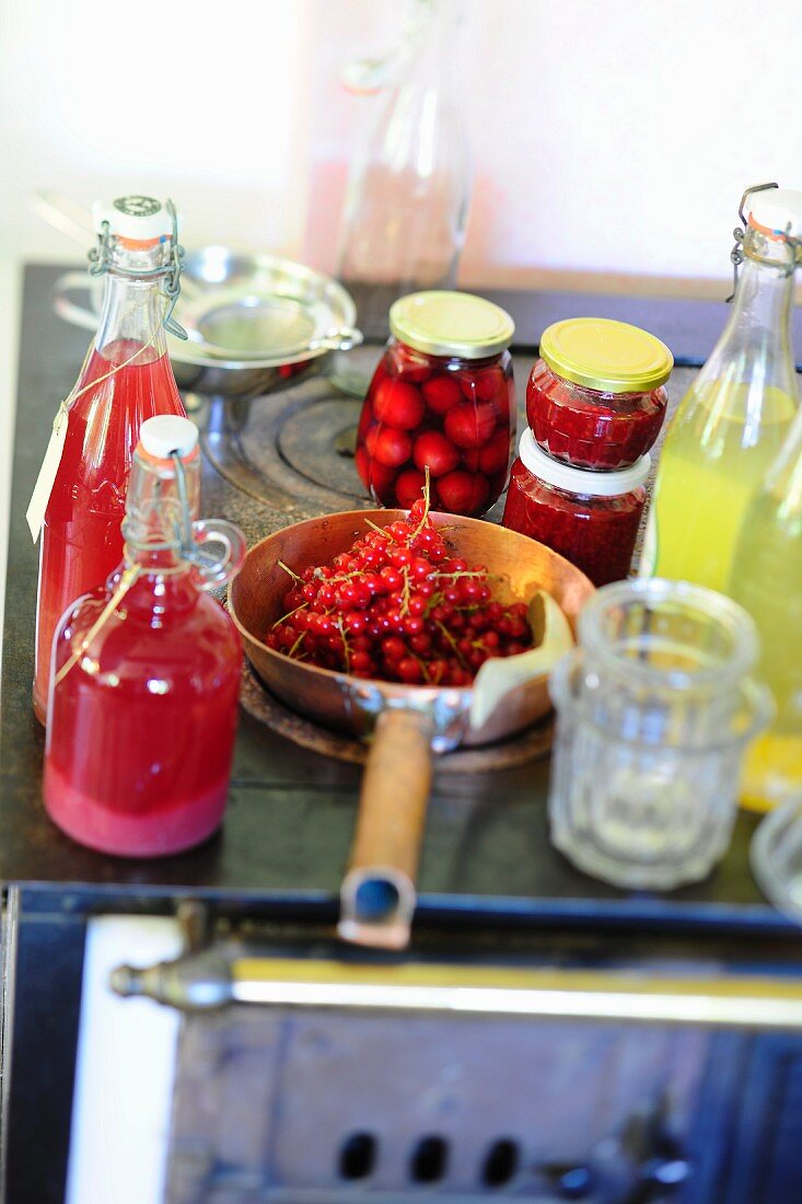 Various homemade fruit juices, preserved fruit and fresh redcurrants on an old stove