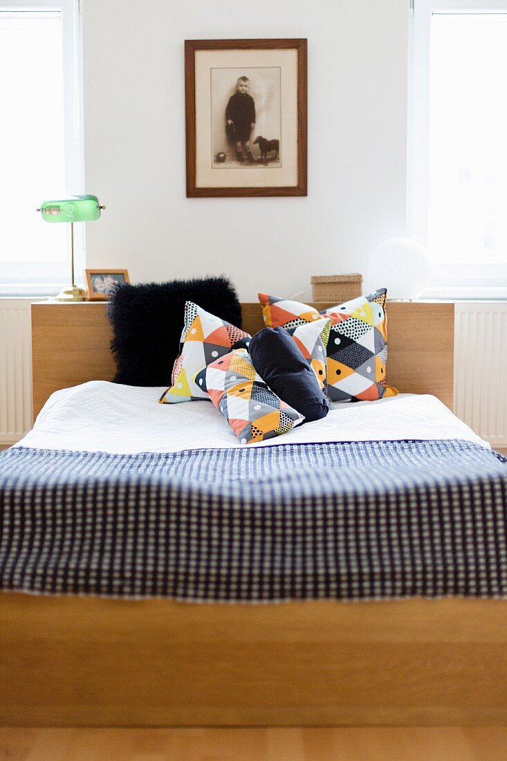 Doppelbett mit Kopfteil, geometrisch gemusterte Kissen und karierte Tagesdecke, gerahmtes Vintage-Kinderfoto an Wand