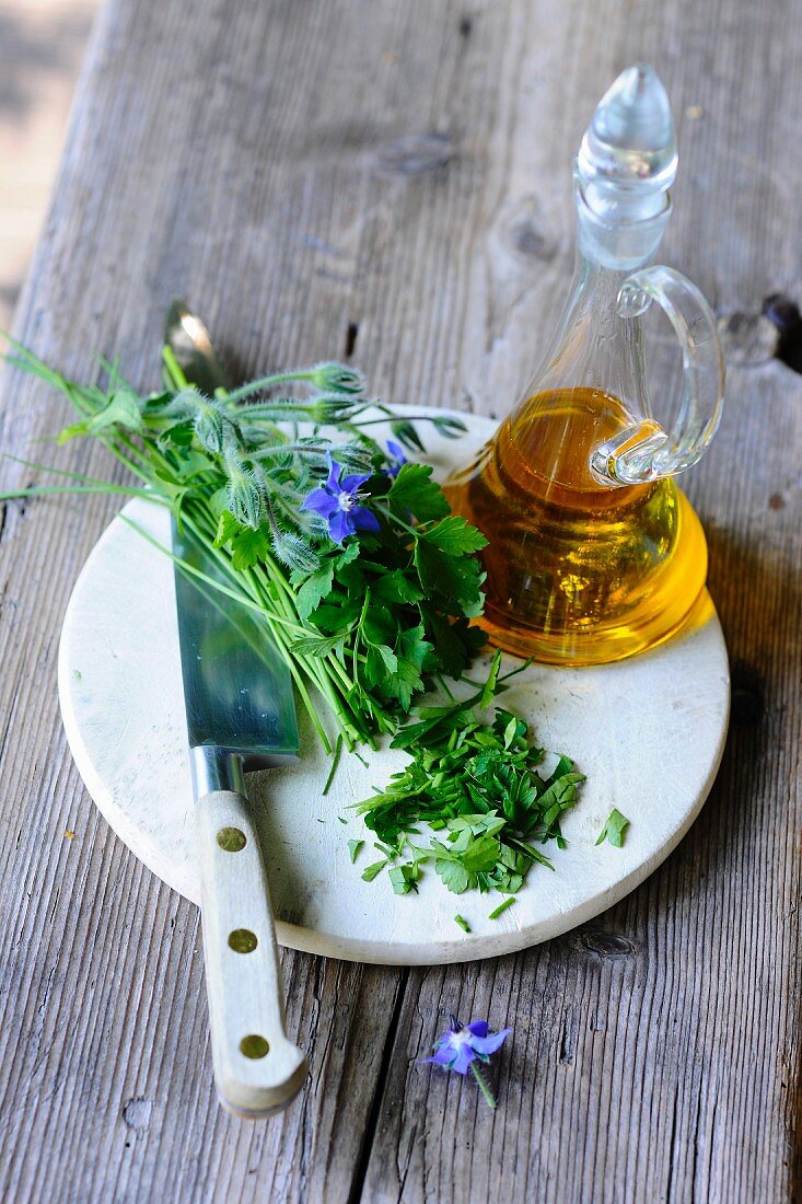Fresh herbs, a knife and a carafe of oil on a wooden table