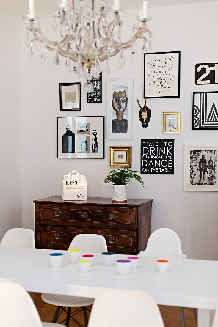 White table, classic shell chairs and antique chest of drawers below collection of pictures on wall in dining area