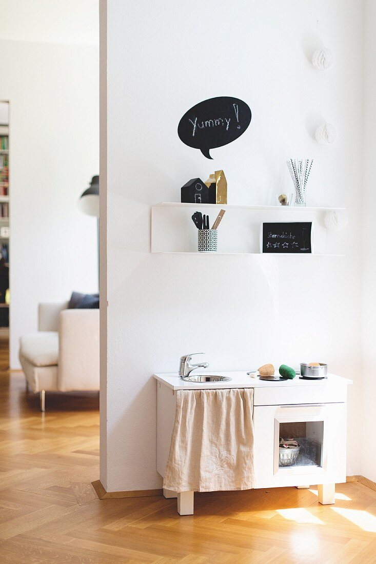 White toy kitchen below shelf in renovated period apartment with herringbone parquet floor