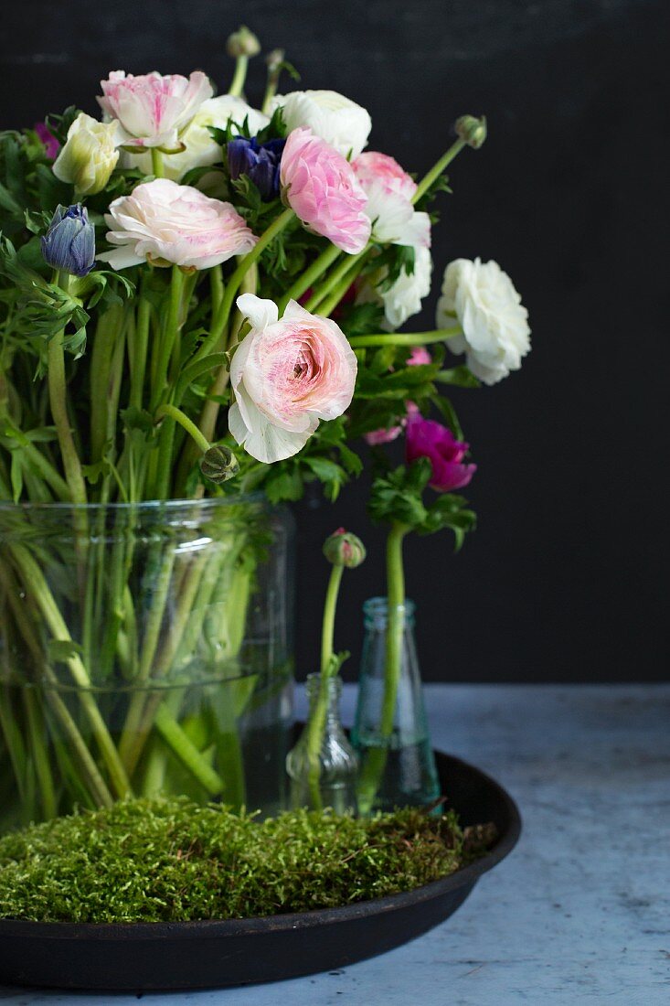 Arrangement of pink ranunculus and anemones in glass vases amongst moss on tray