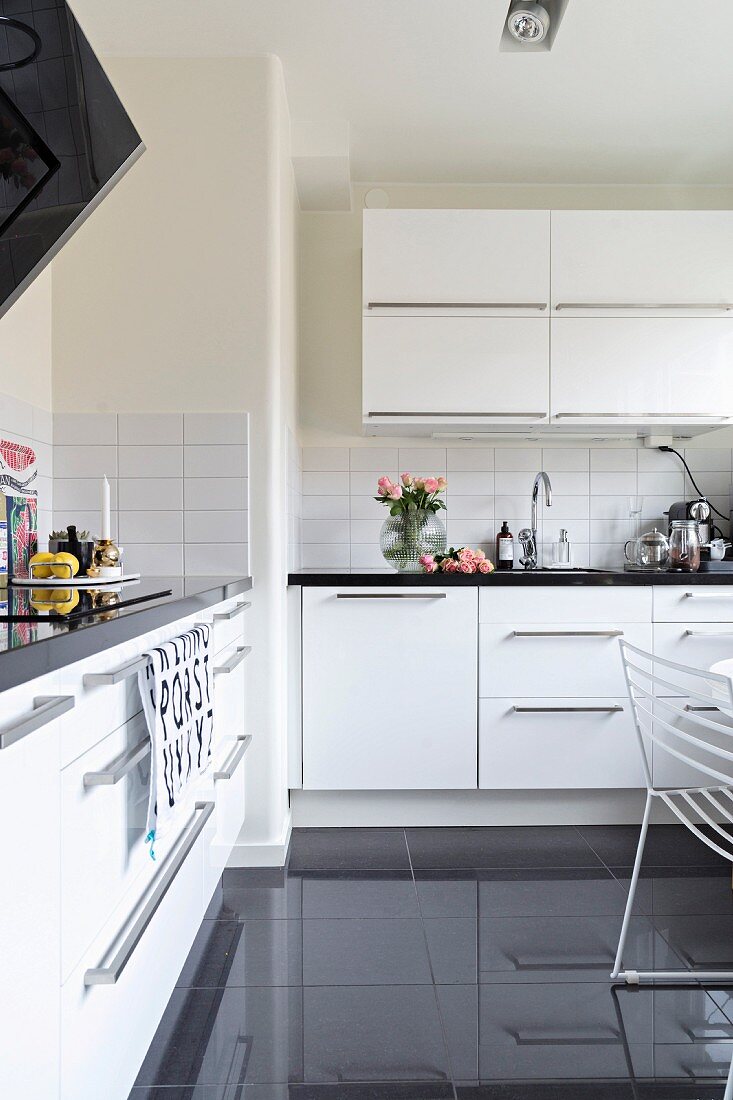 weiße Einbauküche mit Hängeschränken und schwarz glänzendem Fliesenboden