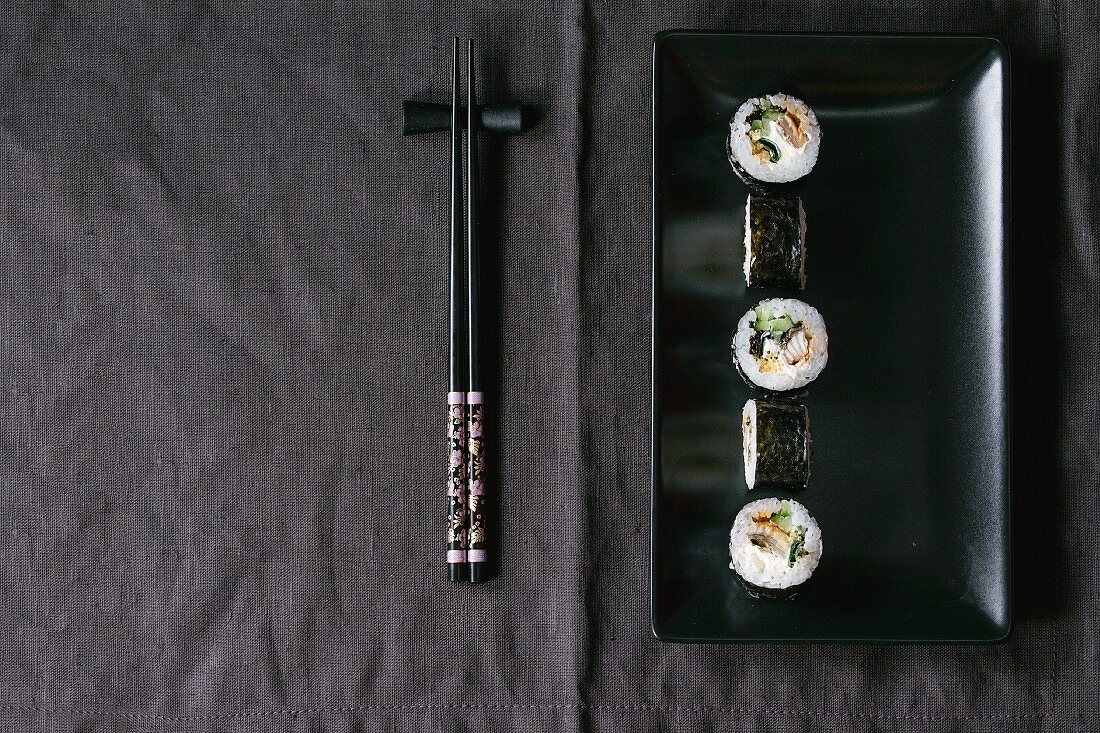 Maki-Sushi auf schwarzem Teller, daneben Essstäbchen (Japan)