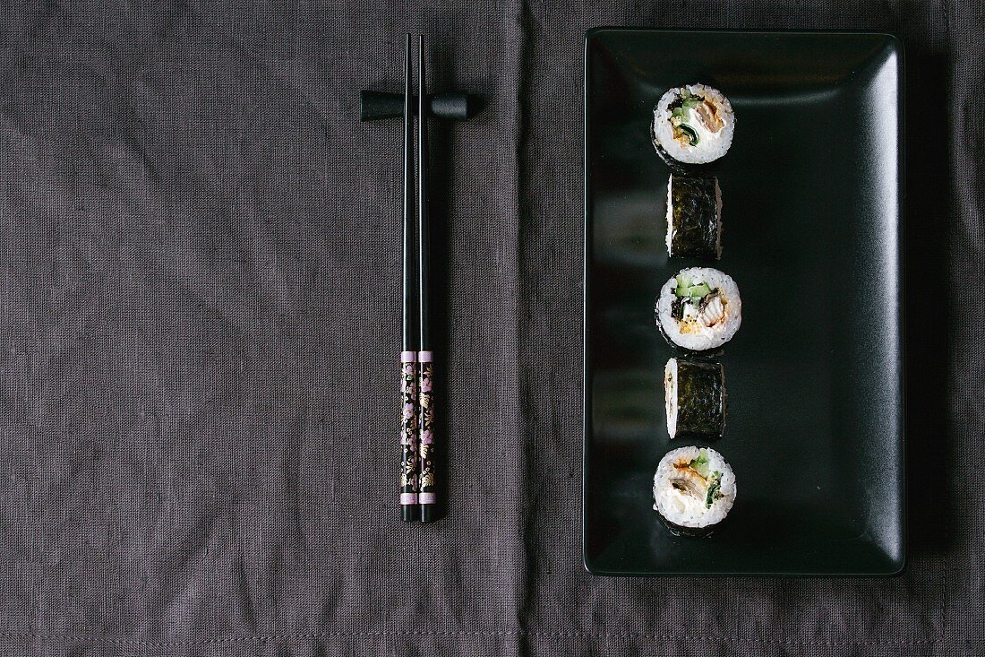 Maki sushi on a black plate next to chopsticks (Japan)