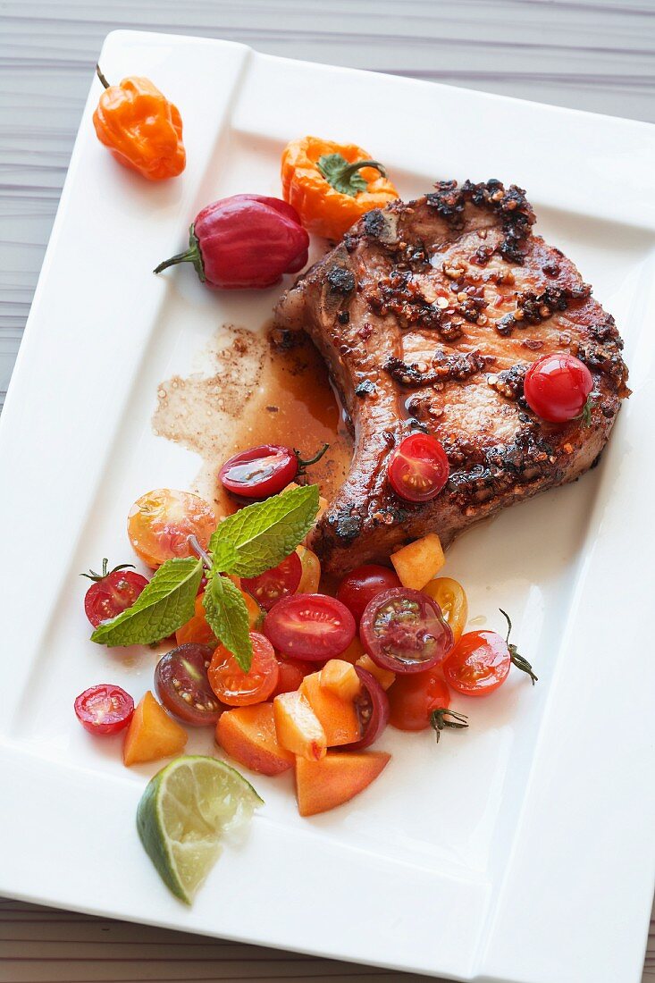 A pork chop with tomato salsa, peaches and peppers