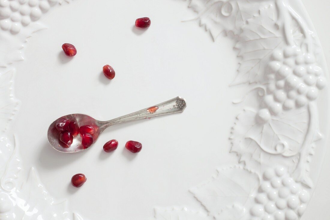 Pomegranate seeds on a spoon and scattered on a white plate