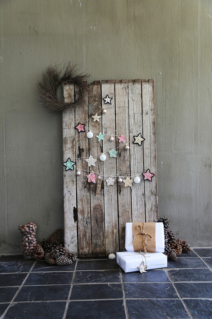 DIY garland made of crocheted doilies and Christmas baubles on a board wall with pinecones and gifts on the floor