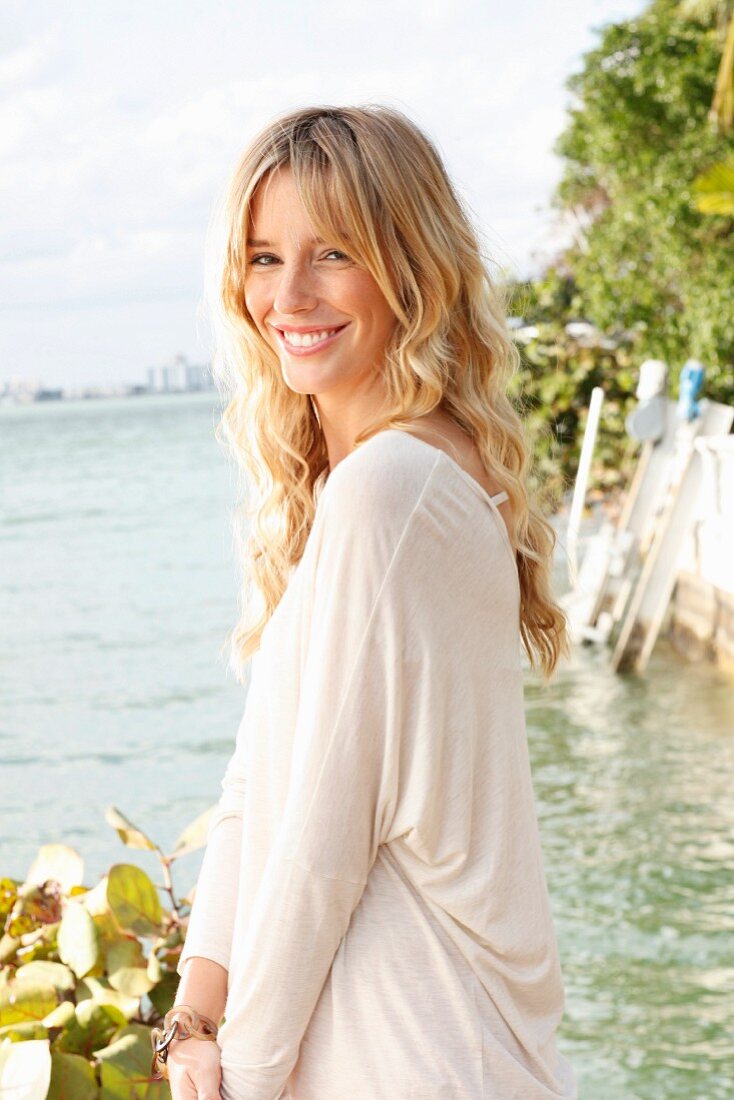 A young blonde woman wearing an light, oversized shirt by the sea