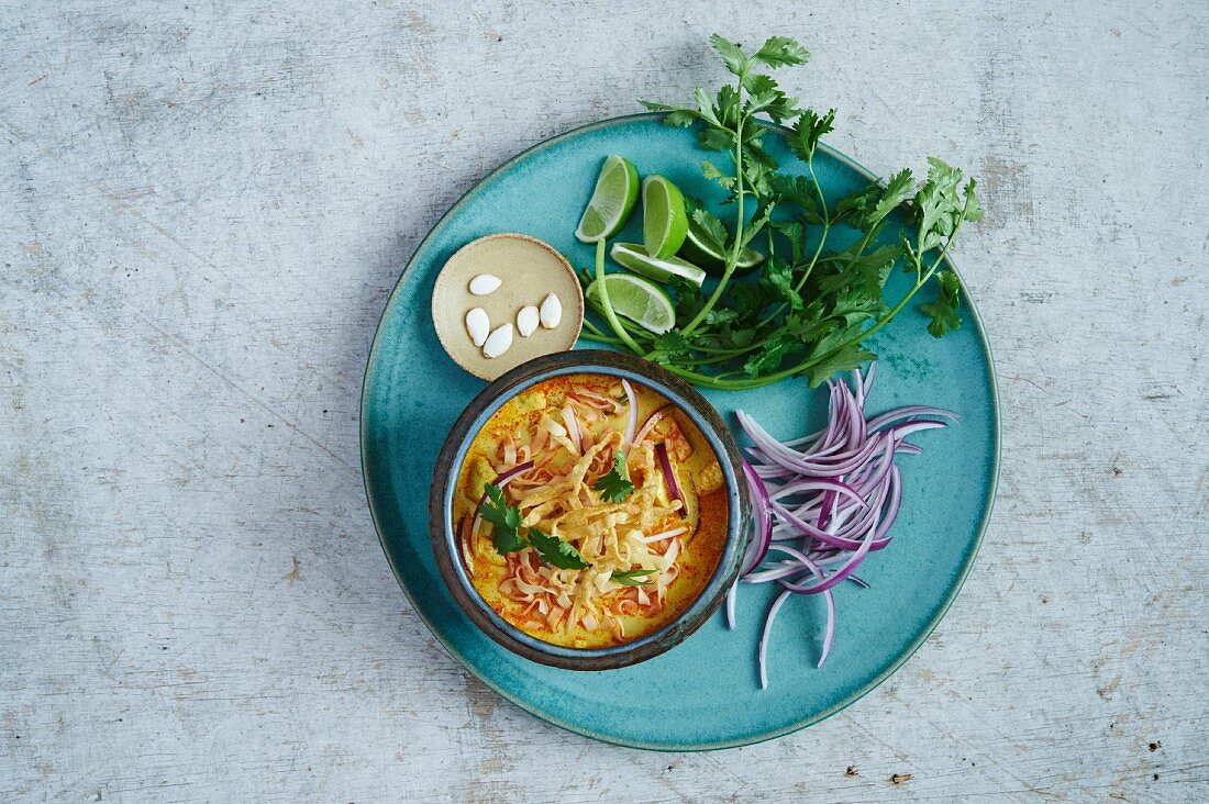 Khao soi soup garnished with red onions, limes, pumpkin seeds and coriander
