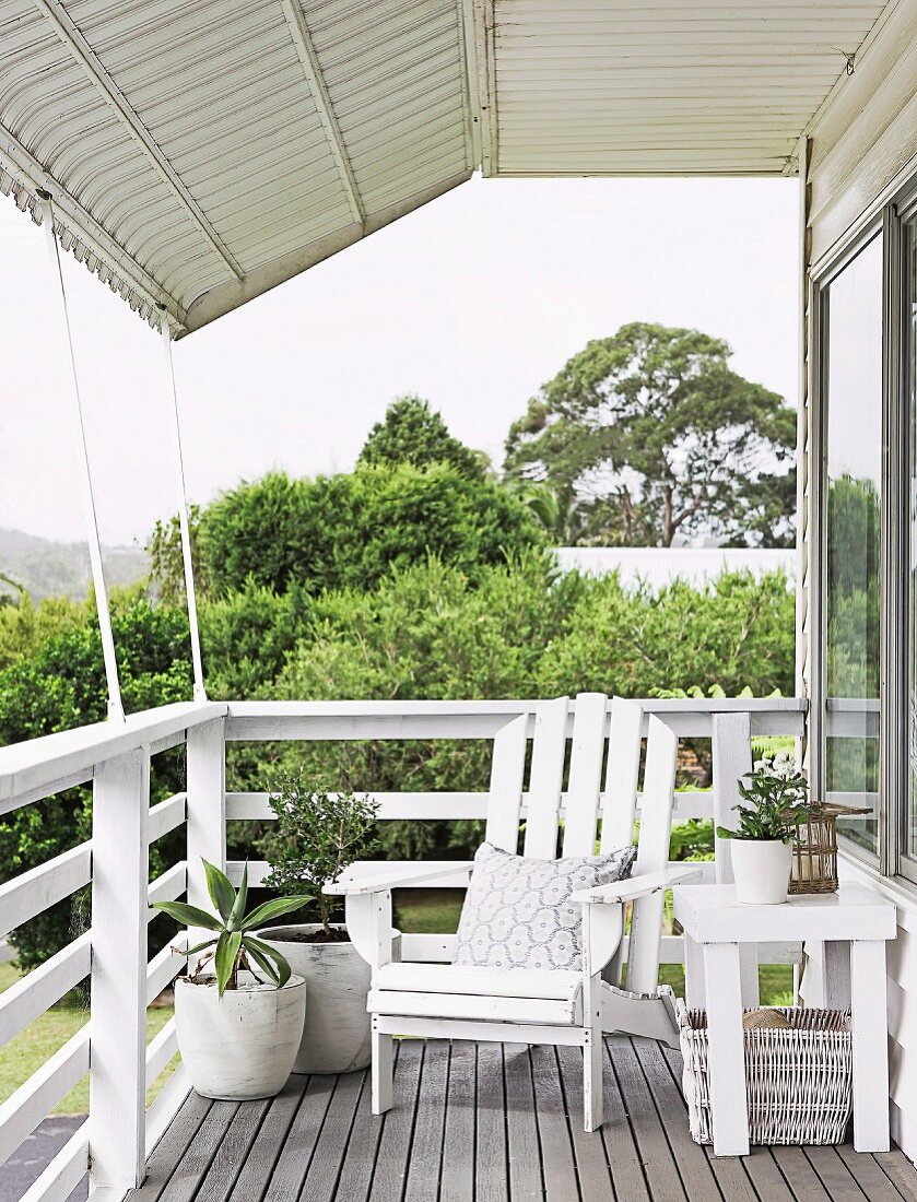 Überdachte Terrasse mit weißem Holzsessel im Landhausstil; Blick über Brüstungsgeländer auf Gartn