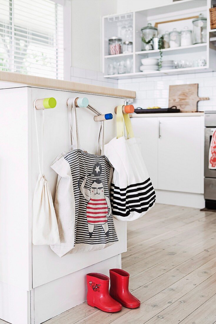 Kindergarderobe an Küchentheke mit Stofftaschen und roten Kindergummistiefeln auf Dielenboden