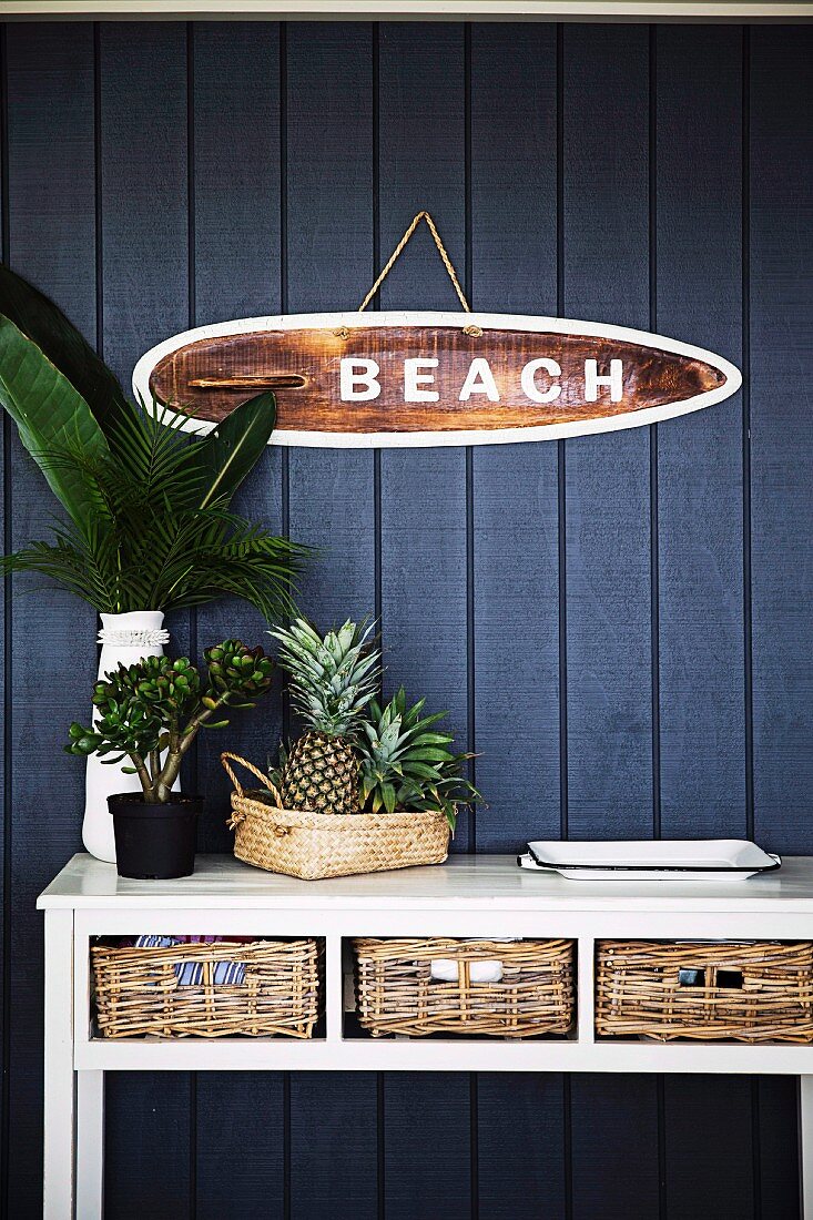 White wall table with storage baskets in front of dark blue wooden wall and maritime sign