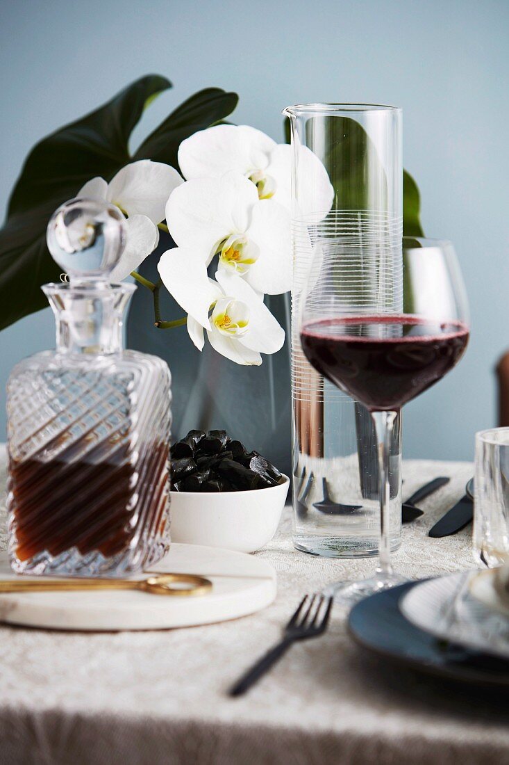 Rotweinglas und Kristallkaraffe, im Hintergrund weiße Orchidee auf Tisch