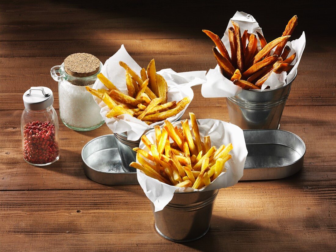 Three types of chips with a salt shaker and pink pepper on a rustic wooden surface